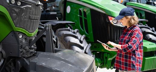Poster - Woman farmer with a digital tablet on the background of an agricultural tractor.