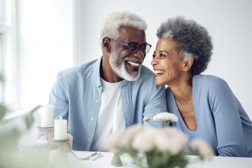 Wall Mural - Smiling, dark-complected stylish Black elderly couple, looking away, at table in kitchen with white walls, in the style of professional stock photography, photo-realistic, high exposure, low contrast