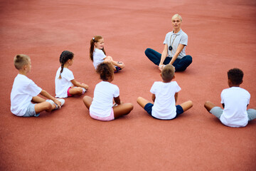 Wall Mural - PE teacher and group of children warming up during exercise class at stadium.