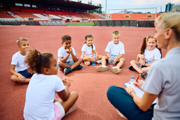 Wall Mural - Multiracial group of kids having exercise class with their coach at stadium.