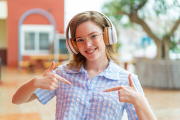 Poster - Young redhead girl headphones at outdoors proud and self-satisfied