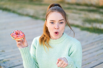 Canvas Print - Young pretty girl holding a donut at outdoors surprised and pointing front