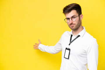 Poster - Young caucasian with ID card isolated on yellow background extending hands to the side for inviting to come