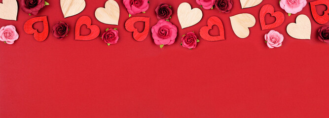 Wall Mural - Valentines Day top border of wooden hearts and roses. Above view on a red banner background. Copy space.