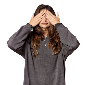 Young Caucasian woman in studio setting afraid covering eyes with hands.