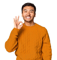 Young Chinese man in studio background cheerful and confident showing ok gesture.