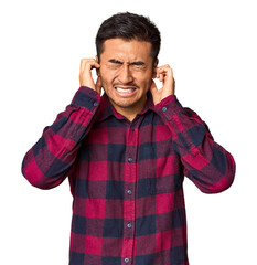 Wall Mural - Young Chinese man in studio background covering ears with hands.