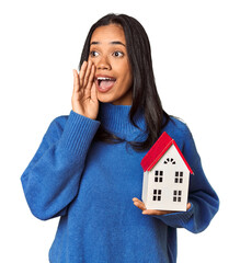 Wall Mural - Young Filipina woman holding a miniature house shouting and holding palm near opened mouth.