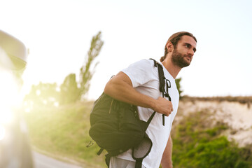 Portrait of young man hiker with backpack standing near his car