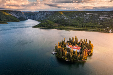 Wall Mural - Visovac, Croatia - Aerial view of Visovac Christian monastery island in Krka National Park on a sunny autumn morning with dramatic golden sunrise and clouds and clear turquoise blue water