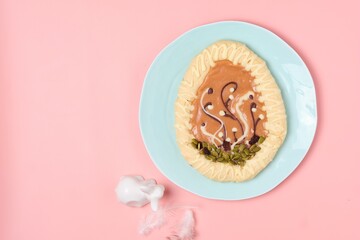 Mazurek, a Polish Easter sweet made from shortcrust pastry in the shape of an egg with Easter decoration on a turquoise plate on a pink background. Polish cuisine.