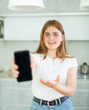 © JackF - in cozy home interior, smiling girl stands and shows interesting photo on screen of mobile phone