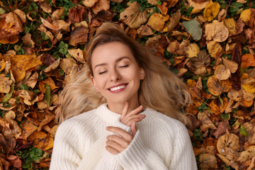 Canvas Print - Smiling woman lying among autumn leaves outdoors, top view