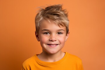 Portrait of a cute little boy with blond hair on a orange background