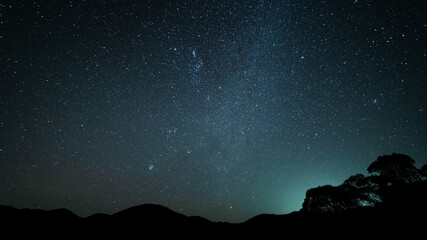 Dark starry night sky in the wilderness with a silhouette of mountains and trees in the background.