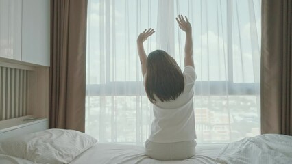 Wall Mural - happy woman stretching on bed after wake up, young adult female rising arms and looking to window in the early morning. fresh relax and have a nice day concepts