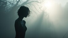  A Woman Standing In A Foggy Forest With Her Hair Blowing In The Wind And The Sun Shining Through The Trees.