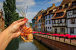 Woman s hand holding a bag of artisanal cookies with half timbered houses above channels of the River Lauch in Petite Venise, Colmar, Alsace, France