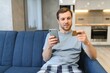 © Serhii - Young man sitting at home paying for food online with smartphone and credit card
