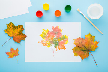 Wall Mural - Painting and copying colorful leaf pattern with gouache color on white paper. Light blue table background. Pastel color. Closeup. Top down view.