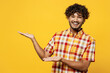 Young happy cool Indian man he wearing shirt casual clothes pointing hands arms aside on workspace area mock up copy space isolated on plain yellow color background studio portrait. Lifestyle concept.