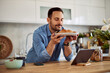 © Jelena - A content young adult man holds a plate of croissants in front of him while leaning on a kitchen counter.