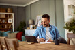 © Jelena - A happy young adult man conducting an online interview on a tablet holding a pen and a sheet of paper in front of him.