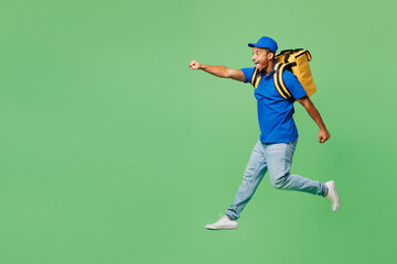 Full body delivery guy employee man wearing blue cap t-shirt uniform workwear yellow thermal food bag backpack work as dealer courier jump high run isolated on plain green background. Service concept.