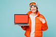 Skier young IT woman in padded windbreaker jacket hat ski goggles mask work use blank screen laptop pc computer travel rest spend weekend winter season in mountains isolated on plain blue background