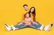 Full body young parents mom dad with child kid girl 7-8 years old wear pink sweater casual clothes sitting with outstretched legs posing kidding isolated on plain yellow background Family day concept