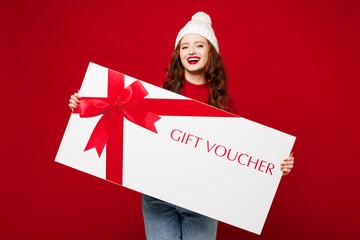 Wall Mural - Young woman she wears knitted sweater white hat casual clothes hold big huge gift certificate coupon voucher card for store isolated on plain red color background studio portrait. Lifestyle concept.