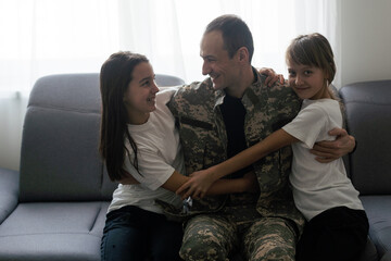  happy positive smiling soldier man in camouflage sitting with his daughter on sofa, looking how his kid grown when he was in army, returning home from war.