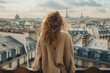 A young girl with long hair is looking at the Paris skyline from the hotel. The tower in the background