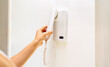 © Barillo_Images - Intercom handset in female hand. Intercom on white wall with copy space.