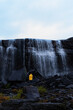 Fotografie von einem Mann der vor dem eindrucksvollen Orvvosfossen Wasserfall in Skandinavien steht, welcher sich durch das vom Regen gefärbten dunklen Gestein seinen Weg bahnt.