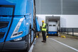 Warehouse receiver standing by blue truck, holding tablet, looking at cargo details, checking delivered items, goods against order.