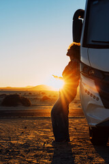 Wall Mural - Happiness and freedom life with woman against camper van and golden sunset in background. People enjoying vanlife and summer holiday vacation with big camping car parked off road. Alone traveler