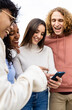 © Xavier Lorenzo - Vertical photo. Happy diverse friends laughing while watching funny videos on smartphone. Young multiracial people having fun using social media networks on mobile phone app. Technology concept