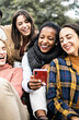 © Xavier Lorenzo - Vertical photo. Happy group of young people sharing video content on social media platform. Millennial multiracial friends using smartphone while sitting outdoors. Youth and technology concept