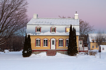 Wall Mural - Sunrise winter view of beautiful patrimonial yellow clapboard house with silver metal Mansard roof and dormer windows, St. Pierre, Island of Orleans, Quebec