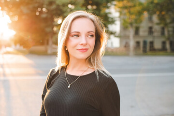 Wall Mural - Smiling blonde woman 24-25 year old walking at city street outdoor over sun light closeup. Looking away.