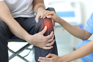 Female doctor diagnosing knee pain of male patient in wheelchair in hospital examination room.