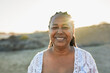 Senior african woman smiling on camera during travel vacation on the beach with sunset in the background