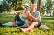© HBS - Retirement with sport and technology. Old man and woman in activewear smiling together while looking on smartphone screen. Positive family using modern gadget while resting after workout at park.