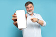 © opolja - Handsome Excited Mature Man Showing Pointing At Empty Smartphone Screen Posing Over Light Blue Studio Background, Smiling To Camera. Check This Out, Cellphone Display Mock Up
