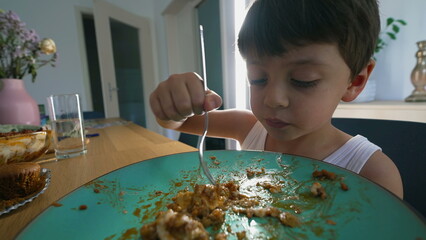 Young boy eating lunch at home meal, child using fork to eat food