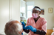 © Marko Geber - Healthcare worker testing senior patient for coronavirus at home