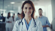 © SkyLine - Female healthcare professional is standing confidently. The focus on the individual against the blurred background of colleagues emphasizes her as the subject of the image, theme of medical leadership