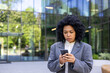 © Liubomir - Upset young African American businesswoman standing outside office building and looking worriedly at phone screen. Close-up photo.