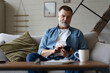 © opolja - Happy smiling senior man using smartphone device while sitting on sofa at home
